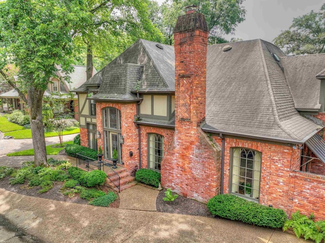 view of front of property with a chimney, brick siding, and roof with shingles