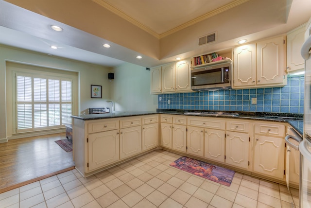 kitchen with visible vents, a peninsula, ornamental molding, stainless steel microwave, and tasteful backsplash