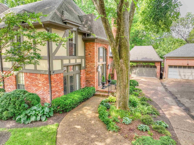 view of front of home with stucco siding, brick siding, a detached garage, and roof with shingles