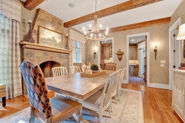 dining room featuring beam ceiling, a notable chandelier, a fireplace, and light wood-type flooring