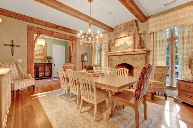 dining space with beamed ceiling, light wood-type flooring, a fireplace, and a chandelier