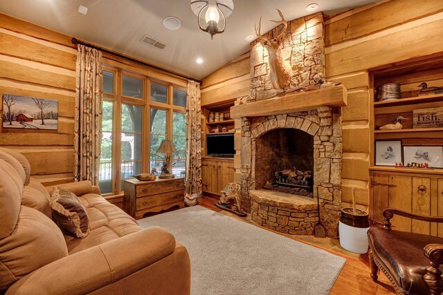 living room featuring built in features, vaulted ceiling, a stone fireplace, and hardwood / wood-style flooring