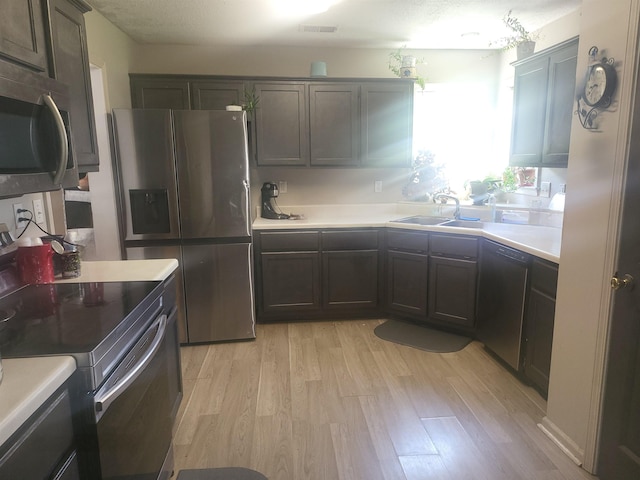 kitchen with dark brown cabinetry, stainless steel appliances, sink, and light hardwood / wood-style floors