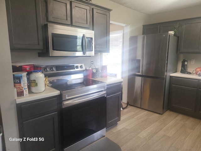 kitchen with stainless steel appliances, dark brown cabinetry, and light hardwood / wood-style flooring