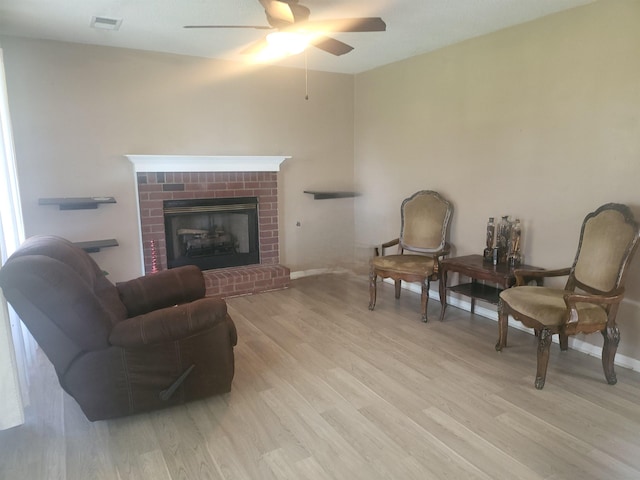 living room with a brick fireplace, light hardwood / wood-style floors, and ceiling fan