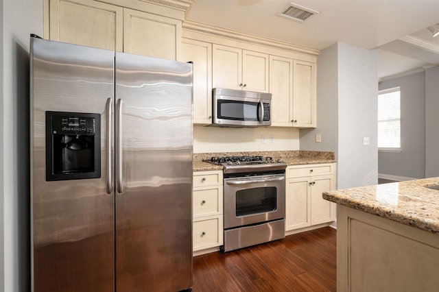 kitchen with light stone counters, dark wood-type flooring, cream cabinetry, and appliances with stainless steel finishes