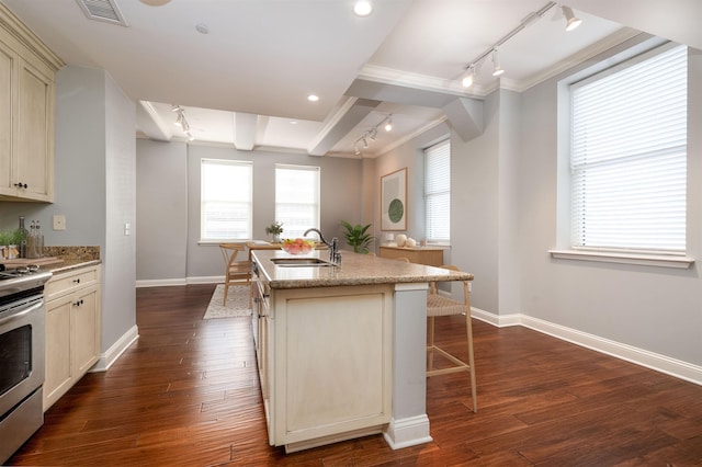 kitchen featuring electric stove, sink, dark wood-type flooring, cream cabinets, and an island with sink