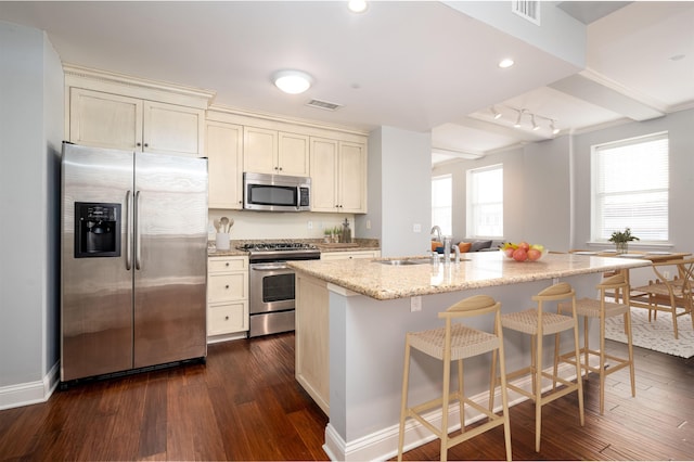 kitchen with appliances with stainless steel finishes, an island with sink, sink, dark hardwood / wood-style flooring, and cream cabinetry