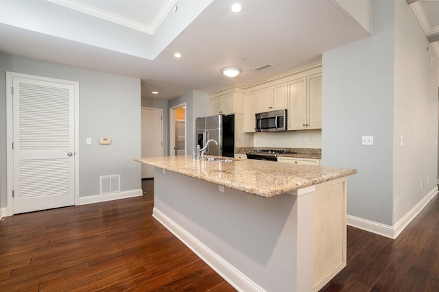 kitchen with sink, dark wood-type flooring, appliances with stainless steel finishes, a kitchen island with sink, and light stone countertops