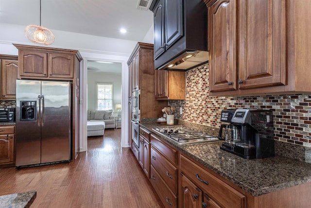 kitchen with stainless steel appliances, backsplash, dark stone countertops, and dark wood-type flooring