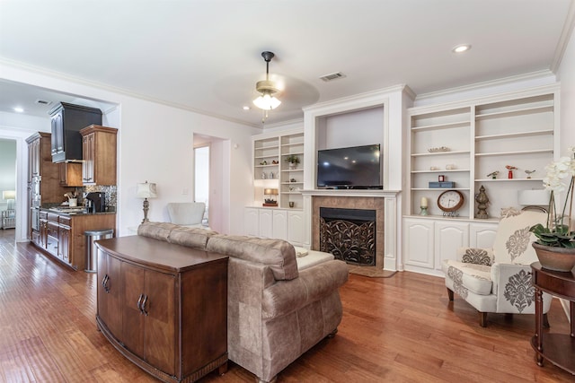 living room featuring ceiling fan, crown molding, hardwood / wood-style floors, and built in features