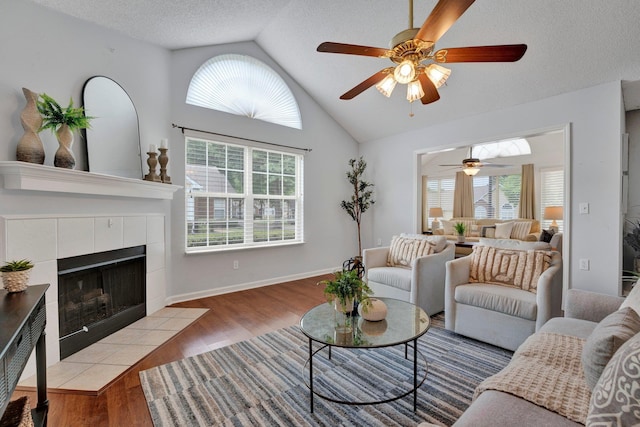 living room featuring ceiling fan, a textured ceiling, light wood-type flooring, vaulted ceiling, and a tile fireplace