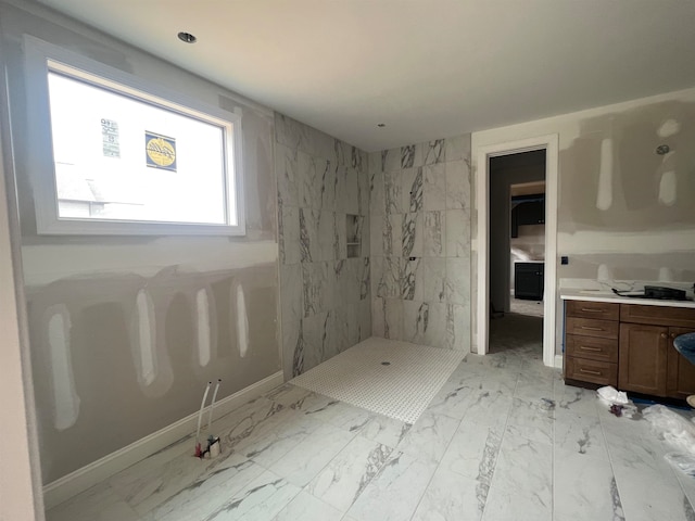 full bathroom with marble finish floor, tiled shower, vanity, and baseboards