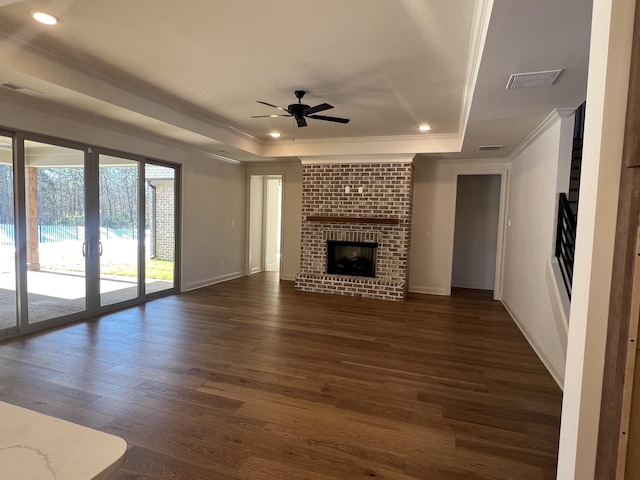 unfurnished living room featuring a brick fireplace, visible vents, a raised ceiling, and dark wood-type flooring