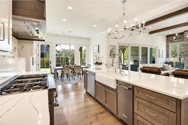 kitchen with sink, light stone counters, hanging light fixtures, light hardwood / wood-style flooring, and stainless steel appliances