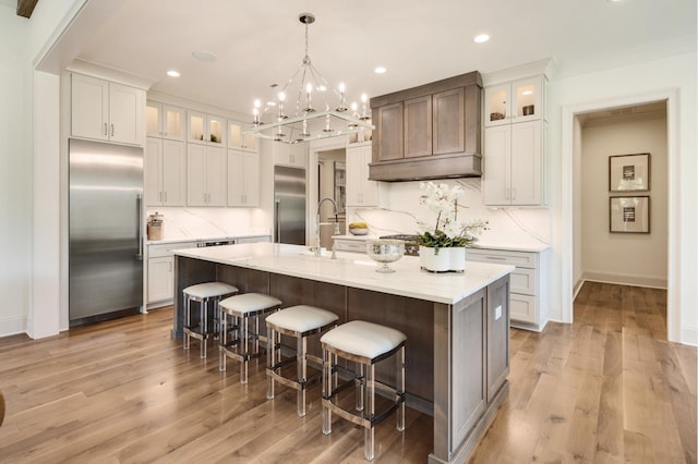 kitchen with a breakfast bar area, appliances with stainless steel finishes, white cabinetry, a center island with sink, and decorative light fixtures