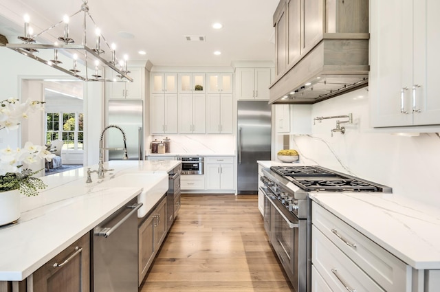 kitchen featuring premium range hood, white cabinets, high end appliances, a large island, and light stone counters