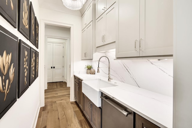 interior space with sink, dishwasher, backsplash, light stone counters, and light hardwood / wood-style floors