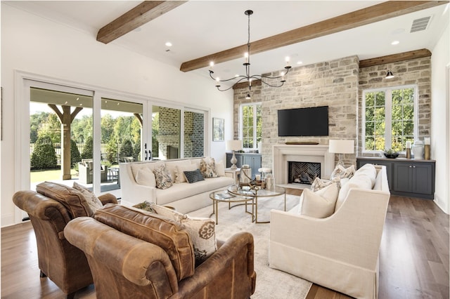 living room featuring beamed ceiling, a large fireplace, wood-type flooring, and a chandelier