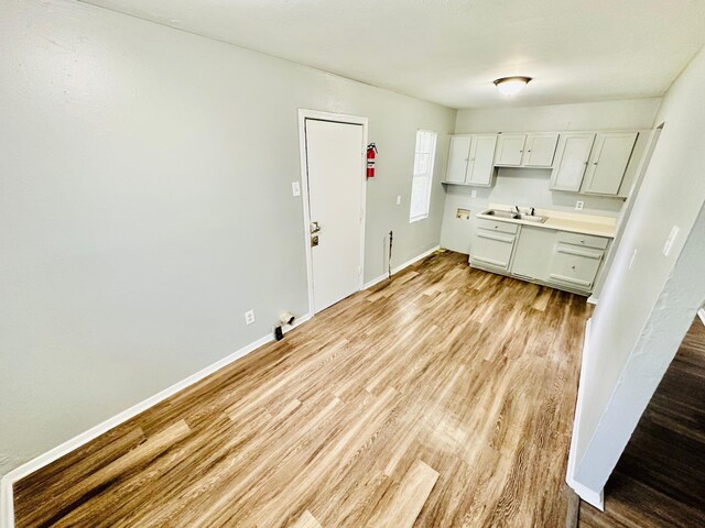 kitchen featuring light countertops, baseboards, light wood-type flooring, and a sink