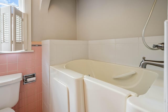 full bath featuring toilet, a garden tub, and tile walls