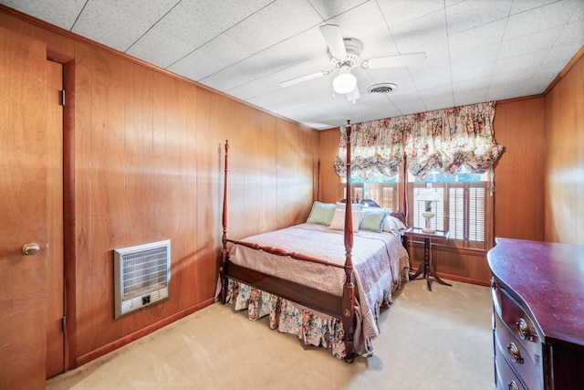 carpeted bedroom with ceiling fan, wooden walls, and heating unit