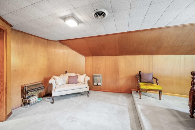 living area with heating unit, wood walls, visible vents, and carpet flooring