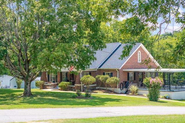 view of front of home featuring covered porch, roof with shingles, a front lawn, and brick siding