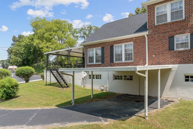 back of house featuring a shingled roof, brick siding, a lawn, and stairs