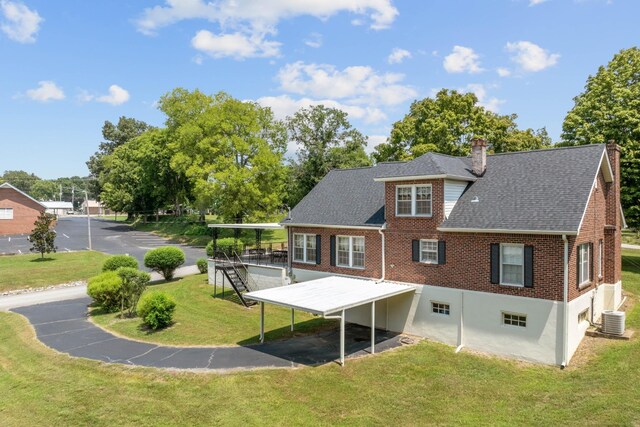 rear view of house with a carport, central air condition unit, and a lawn