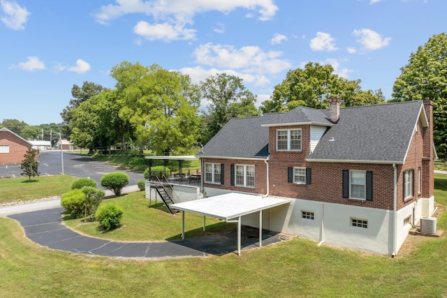 back of house with a yard, brick siding, a chimney, and central air condition unit