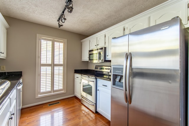 kitchen with a textured ceiling, light hardwood / wood-style flooring, white cabinets, and appliances with stainless steel finishes