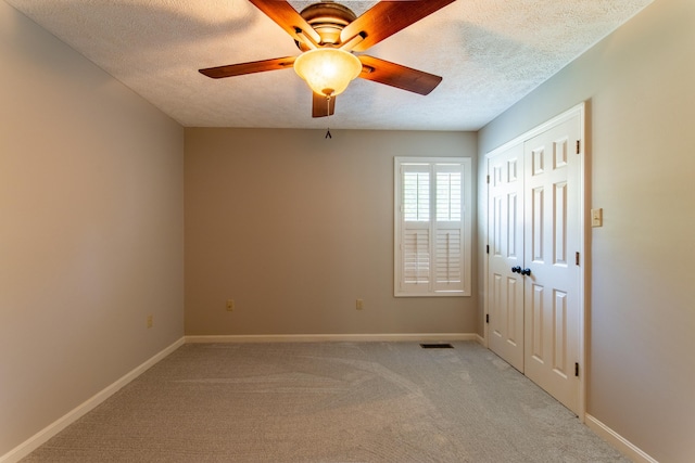 empty room featuring ceiling fan, light colored carpet, and a textured ceiling