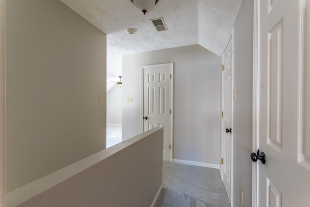 hallway with lofted ceiling, a textured ceiling, and carpet flooring