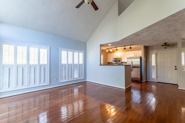 unfurnished living room featuring high vaulted ceiling, dark wood-type flooring, track lighting, and a textured ceiling