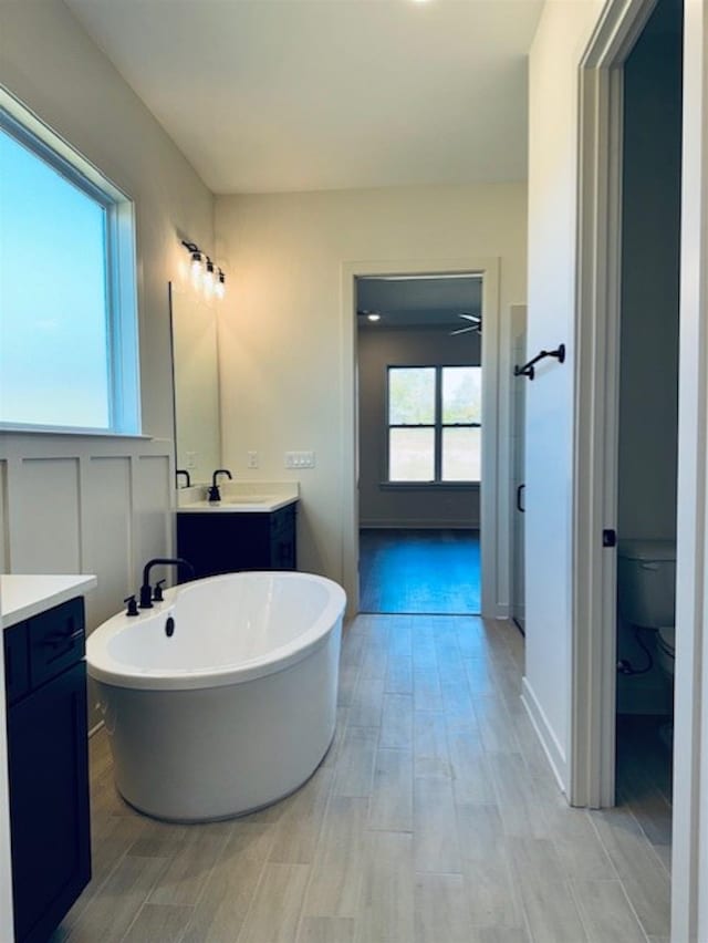 full bathroom featuring wood tiled floor, a freestanding tub, vanity, and toilet