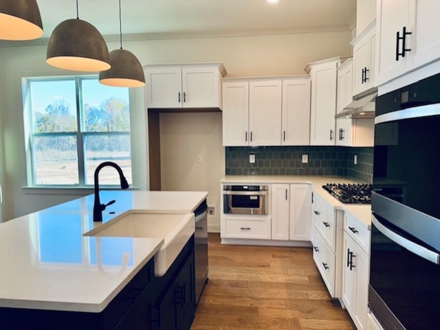 kitchen with hanging light fixtures, under cabinet range hood, white cabinetry, and light countertops