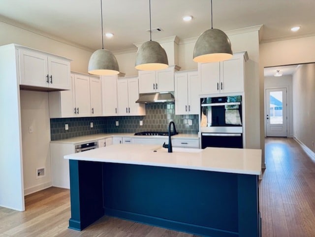 kitchen with light countertops, a center island with sink, under cabinet range hood, and white cabinetry