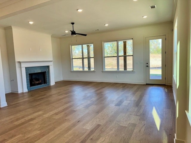 unfurnished living room featuring visible vents, a tile fireplace, ornamental molding, wood finished floors, and recessed lighting