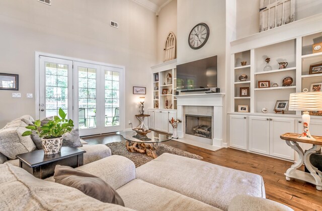 living room featuring a tiled fireplace, built in features, hardwood / wood-style flooring, and a high ceiling