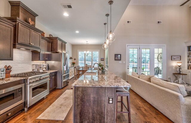 kitchen with a breakfast bar area, stainless steel appliances, light stone countertops, decorative backsplash, and dark wood-type flooring