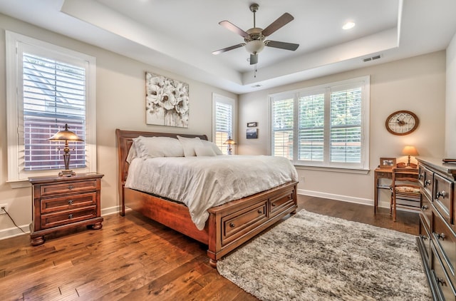 bedroom featuring a tray ceiling, dark wood-type flooring, ceiling fan, and multiple windows