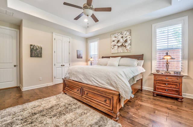 bedroom with ceiling fan, dark wood-type flooring, a raised ceiling, and a closet