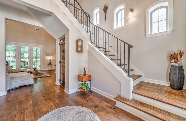 stairs with a towering ceiling, plenty of natural light, and wood-type flooring