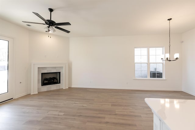 unfurnished living room featuring light wood-type flooring, a fireplace, baseboards, and ceiling fan with notable chandelier