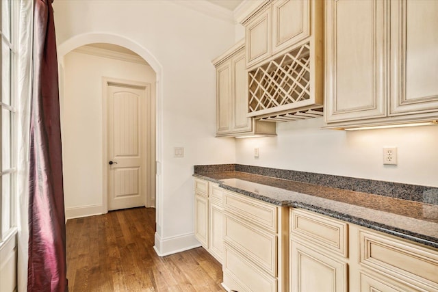 kitchen with crown molding, dark hardwood / wood-style floors, dark stone counters, and cream cabinetry