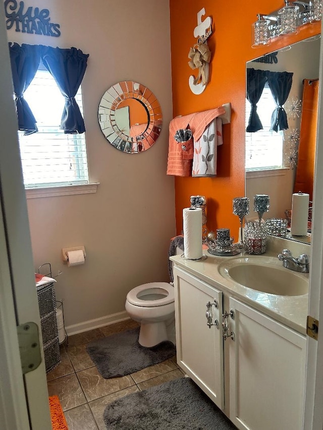 half bathroom with toilet, tile patterned floors, baseboards, and vanity