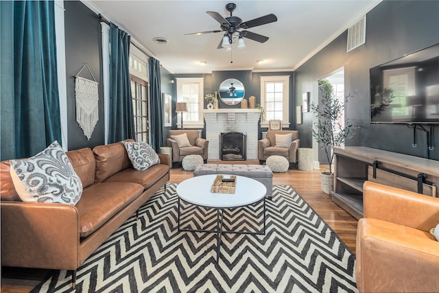 living room with ceiling fan, a fireplace, ornamental molding, and hardwood / wood-style floors