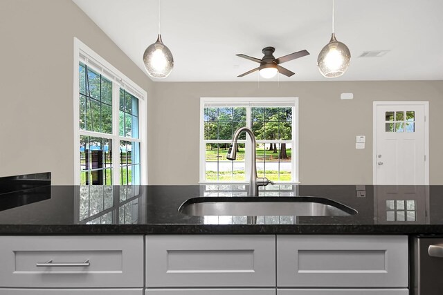 kitchen featuring dark stone countertops, sink, pendant lighting, and a wealth of natural light