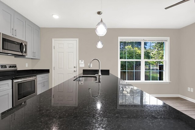 kitchen featuring dark stone countertops, hanging light fixtures, appliances with stainless steel finishes, wood-type flooring, and sink